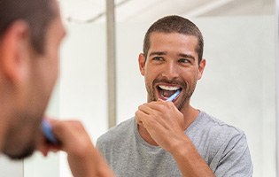 Man smiling while brushing his teeth in bathroom