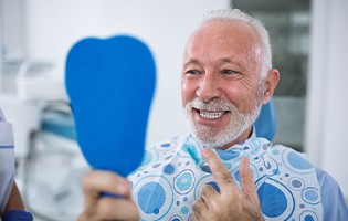 Man smiling while looking at reflection in handheld mirror