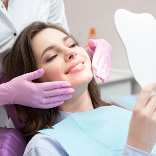 Young woman smiling in mirror after cosmetic dentistry in Fair Oaks