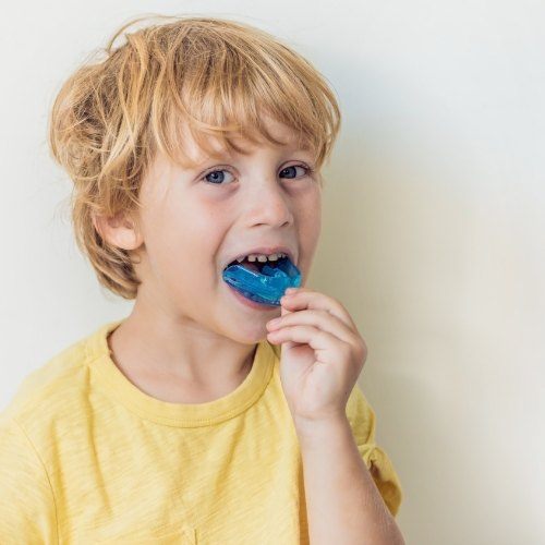 Young boy placing a blue athletic mouthguard on his teeth