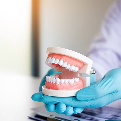 Blue-gloved hands holding an artificial set of teeth