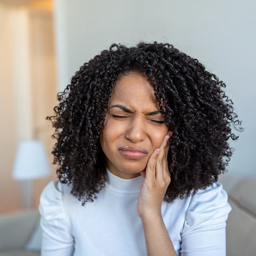 Woman in light blue shirt holding side of her face in pain