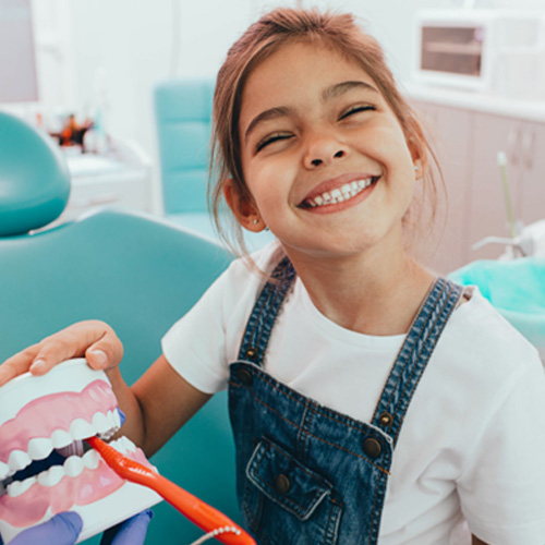  a child being shown how to brush her teeth at a dental office