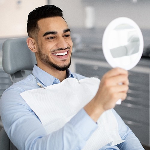 Man in dental chair admiring his smile in mirror