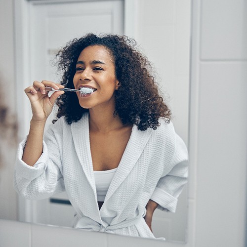 Woman brushing teeth in front of bathroom mirror