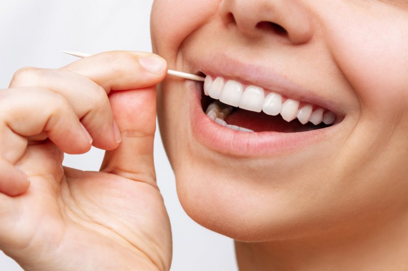 A smiling woman using a toothpick on her teeth