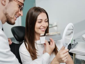 Dentist holding veneers up to patient while she smiles into mirror.